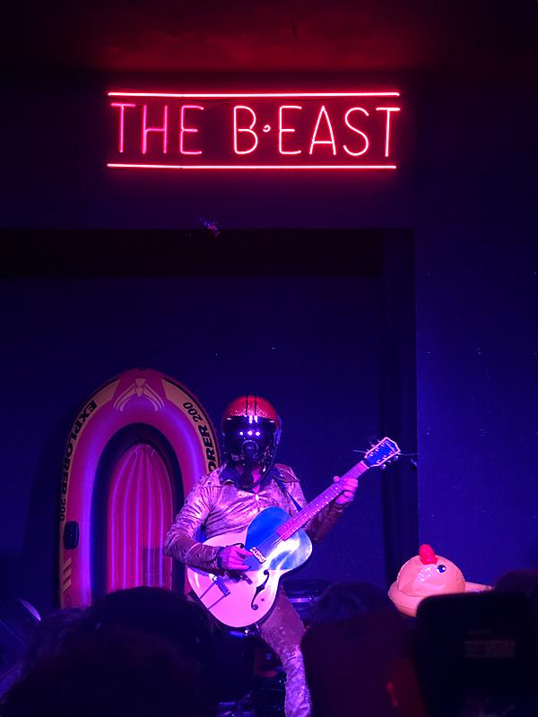 Bob Log III at The B-East | A man plays guitar with a motorcycle helmet and a telephone receiver attached to the front.